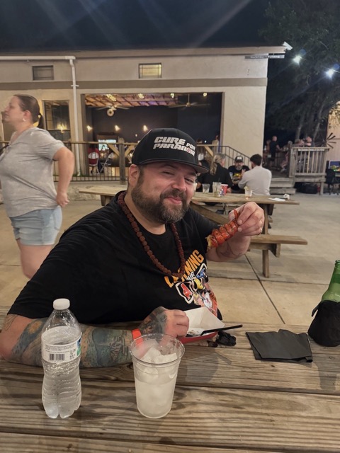 A festival-goer eating a grilled lobster tail at a picnic table at Rocklobster Fest, Josabi's, Helotes, Texas