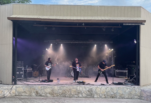 A band performing under stage lights and haze on the outdoor amphitheater stage at Rocklobster Fest, Josabi's, Helotes, Texas